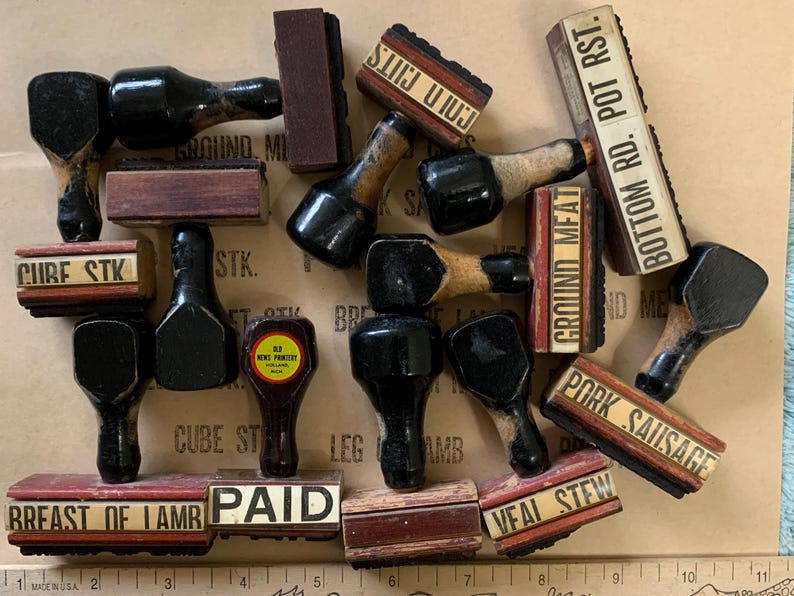 Puede incluir: Una colecci&oacute;n de sellos de madera y goma vintage con varias etiquetas, incluyendo "Ground Meat", "Bottom Rd. Pot Rst", "Pork Sausage", "Paid", "Breast of Lamb" y "Veal Stew".