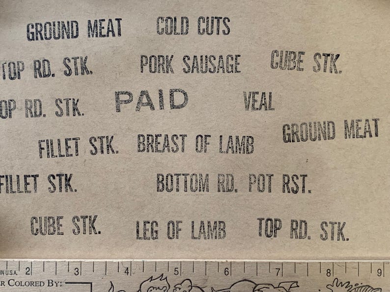 Puede incluir: Primer plano de una bolsa de papel marr&oacute;n con sellos de tinta negra que enumeran varios tipos de carne, incluyendo carne molida, embutidos, salchichas de cerdo, bistec en cubos, bistec redondo superior, bistec de filete, pecho de cordero, ternera, asado de fondo redondo y pierna de cordero. La bolsa tambi&eacute;n tiene un sello que dice "PAGADO".