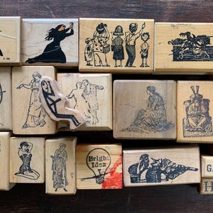 May include: A collection of rectangular wooden rubber stamps featuring various black ink illustrations, including figures, a lightbulb with the text Bright Idea, and small blocks with the words Cool, Out, Sex, Fuck, Gasp, and Huh? arranged in a grid.
