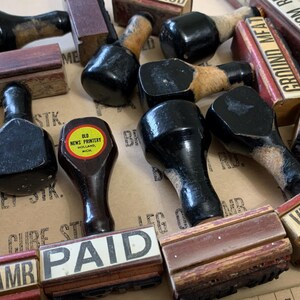 Puede incluir: Una colecci&oacute;n de sellos de goma vintage de madera con almohadillas de tinta negra. Los sellos presentan palabras como "Pagado", "Carne molida", "Redondo de fondo", "Cerdo" y "Bistec de ternera". Un sello tiene una etiqueta amarilla que dice "Old News Printery, Holland, Mich."