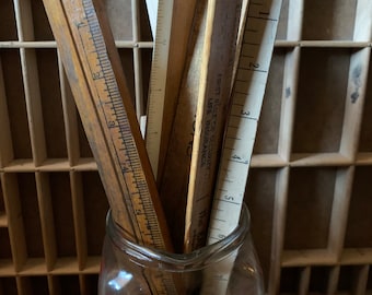 Puede incluir: Una colección de reglas de madera vintage con marcas de medición visibles y texto impreso, incluida la frase First Rule of Security Life Insurance, colocadas verticalmente dentro de un frasco de vidrio transparente con borde redondeado.