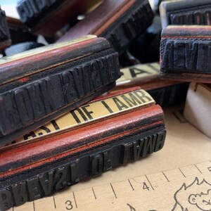 Puede incluir: Una colecci&oacute;n de sellos de goma de madera vintage con varias frases, incluyendo "HOWEVER", "BEST OF I AM" y "PREVAL OF WAR". Los sellos est&aacute;n dispuestos en una pila sobre una superficie marr&oacute;n.