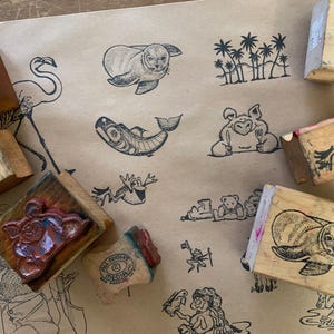 Peut inclure: Ensemble de tampons en caoutchouc vintage avec divers motifs animaliers et naturels. Les tampons en bois présentent des images de phoque, de poisson, de grenouille et de palmiers. Ils sont disposés sur un fond de papier brun avec d'autres illustrations.