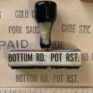 Puede incluir: Un sello de madera con un mango negro y una superficie rectangular blanca. El sello dice "BOTTOM RD. POT RST."