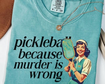 May include: Seafoam green t-shirt with the text "pickleball because murder is wrong" and a retro illustration of a woman holding a pickleball paddle.