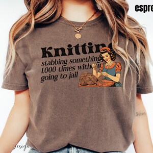 May include: A brown t-shirt with the text "Knitting: stabbing something 1,000 times without going to jail" and a vintage illustration of a woman knitting.