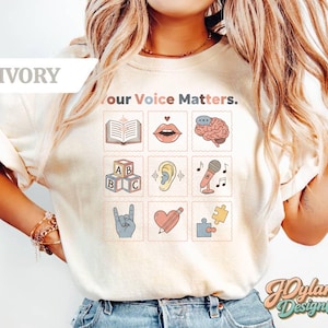 May include: Ivory-colored t-shirt with the text "Your Voice Matters." and a grid of illustrated stamps. The stamps feature images of a book, lips, a brain, ABC blocks, an ear, a microphone, a hand, a heart, and a puzzle piece.