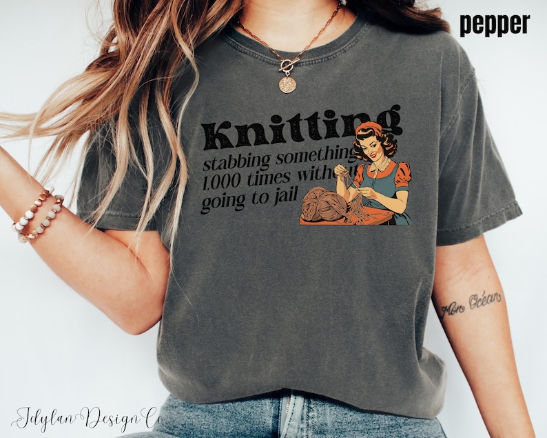 May include: A gray t-shirt with a vintage-style graphic that says "Knitting stabbing something 1,000 times with going to jail". The graphic features a woman knitting.