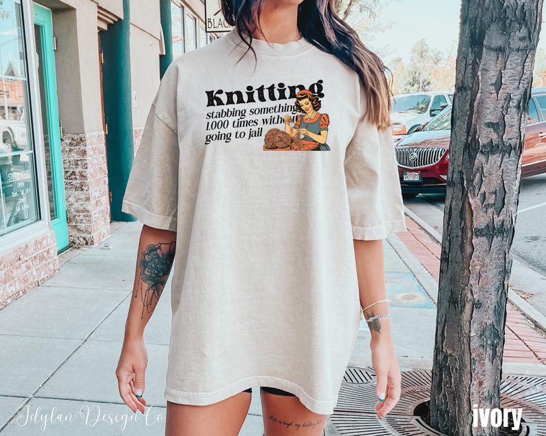 May include: A woman wearing a light beige t-shirt with the text "Knitting stabbing something 1000 times without going to jail" and a cartoon image of a woman knitting.