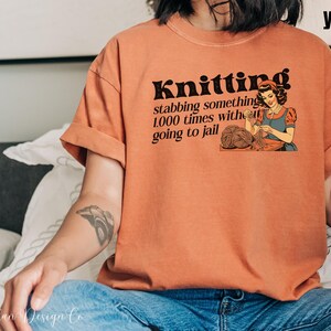 May include: A woman wearing a burnt orange t-shirt with the text "Knitting stabbing something 1,000 times without going to jail" and a vintage illustration of a woman knitting.
