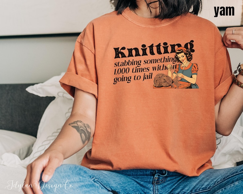 May include: A woman wearing a burnt orange t-shirt with the text "Knitting stabbing something 1,000 times without going to jail" and a vintage illustration of a woman knitting.