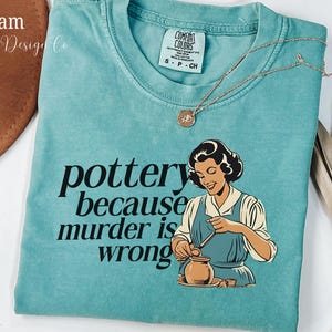 May include: A teal blue t-shirt with the text "pottery because murder is wrong" and a cartoon image of a woman making pottery.