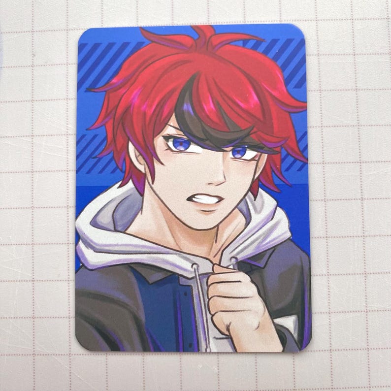 Puede incluir: Tarjeta rectangular con una ilustraci&oacute;n de estilo anime de una persona con cabello rojo y ojos azules. El personaje lleva una chaqueta negra con una sudadera con capucha blanca. El fondo es azul con l&iacute;neas blancas diagonales.