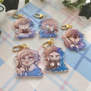 Peut inclure: Cinq porte-clés de personnages d'anime colorés avec des anneaux dorés. Chaque porte-clés présente un personnage différent avec une expression et une pose uniques. Les porte-clés sont en acrylique transparent et ont une finition brillante.