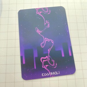 Puede incluir: Una tarjeta rectangular con esquinas redondeadas, con un fondo oscuro con un degradado p&uacute;rpura y azul. Un dise&ntilde;o rosa y ondulado fluye verticalmente. La palabra "EGGTRAOLI" est&aacute; impresa en blanco en la parte inferior.