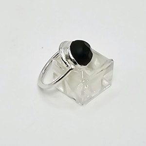 Puede incluir: Un anillo de plata con una piedra preciosa negra. El anillo está en un expositor transparente.
