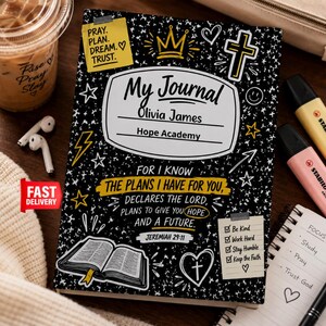 Op de afbeelding: Een zwart dagboek met witte spikkels, een gele kroon, een kruis en de tekst My Journal, Olivia James, Hope Academy. Het bevat het bijbelvers Jeremia 29:11, een checklist met Be Kind, Work Hard, Stay Humble, Keep the Faith en een illustratie van een boek.
