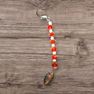 Op de afbeelding: Een sleutelhanger met witte en oranje kralen en een zilveren voetbalbedel.