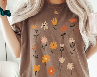 May include: A brown oversized t-shirt with a floral print featuring yellow, orange, and pink flowers. The flowers are stylized and abstract.