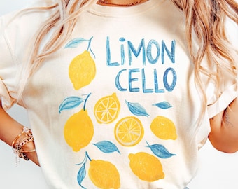 May include: Cream-colored t-shirt featuring a "Limoncello" design. The design includes yellow lemons, blue leaves, and the text "Limoncello" in blue. The shirt has short sleeves and a relaxed fit.