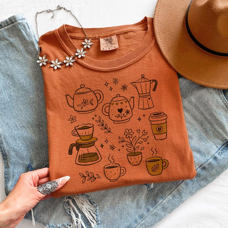 Peut inclure: Un t-shirt orange avec un th&egrave;me caf&eacute; et th&eacute;. Le t-shirt pr&eacute;sente des illustrations de th&eacute;i&egrave;res, de tasses &agrave; caf&eacute;, d'une cafeti&egrave;re et de plantes. Le t-shirt est associ&eacute; &agrave; un chapeau marron et &agrave; un jean bleu.