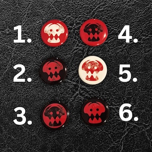 May include: Six round buttons with a skull design in red and white on a black background. The buttons are numbered 1 through 6. The skull design is a stylized, cartoonish image.