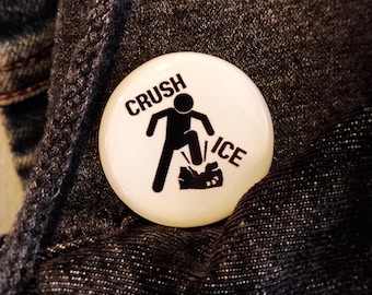 May include: A circular white pinback button featuring a black graphic of a stick figure stomping on a block of ice. The text CRUSH is printed above the figure and the word ICE is printed to the right of the figure in a bold black font.
