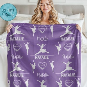 May include: Purple fleece blanket with a white silhouette of a ballerina and the name Natalie repeated throughout the design. The blanket has a white heart with the text #danclife in the center.