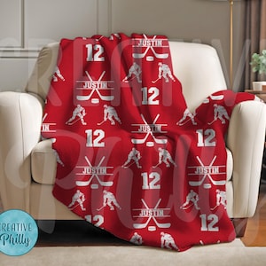 May include: Red fleece blanket with a hockey player and stick pattern. The blanket features the name "Justin" and the number "12" repeated throughout.