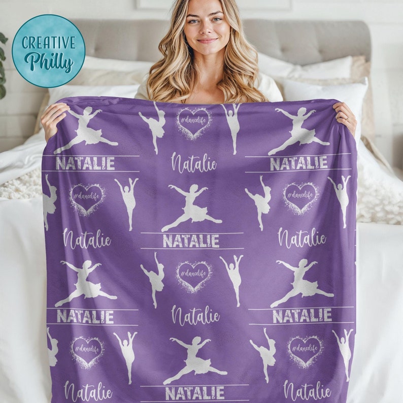 May include: Purple fleece blanket with a white silhouette of a ballerina and the name Natalie repeated throughout the design. The blanket has a white heart with the text #danclife in the center.