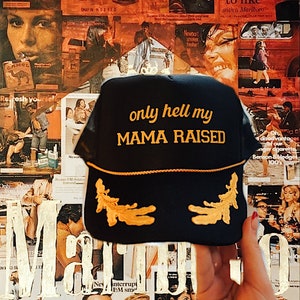 May include: A black mesh trucker hat with a gold embroidered design. The hat has the text "only hell my MAMA RAISED" in gold lettering.
