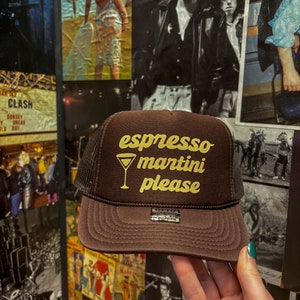 May include: A brown and black trucker hat with a gold embroidered design that says "espresso martini please" and a small martini glass graphic.