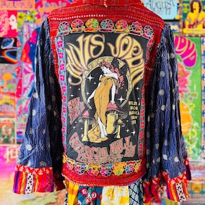 Könnte beinhalten: Eine Jacke mit rotem Oberteil und einem zentralen schwarzen Einsatz, der eine Janis Joplin-Grafik, Text und Pilzillustrationen zeigt. Die Ärmel sind dunkelblau mit einem strukturierten Muster und der Saum hat eine bunte Blumenborte.