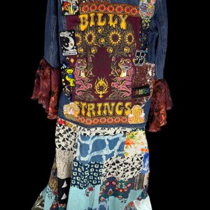 以下が含まれることがあります： BILLY STRINGSの文字、ヒマワリ、カエルの大きな中央パッチと、月やキノコなどの小さなパッチが施された青いデニムジャケット。ジャケットにはフリル付きの袖とパッチワークスカートが取り付けられています。