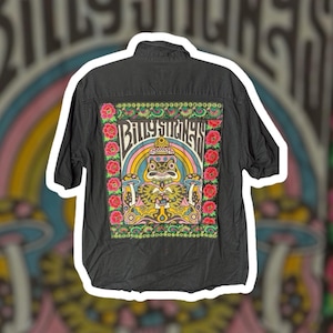 May include: A black short-sleeve button-down shirt featuring a large rectangular patch on the back. The patch displays a colorful graphic of a frog, mushrooms, and rainbows with the text "Billy Strings" in a stylized font, framed by floral borders.