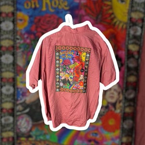May include: A dusty rose short-sleeve button-down shirt featuring a large rectangular graphic patch on the back. The patch displays a colorful psychedelic collage with the text "Ramble on Rose" and "The Beatles" surrounded by a patterned border.