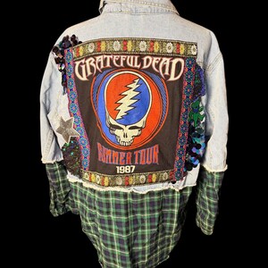 Könnte beinhalten: Eine hellblaue Jeansjacke mit einem großen Grateful Dead Summer Tour 1987 Aufnäher auf der Rückseite. Die Jacke hat unten Stoffeinsätze mit dunkelgrünem und marineblauem Karomuster, dekorative Pailletten, einen Sternaufnäher und Blumenborte.