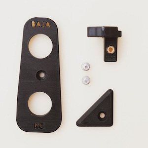 May include: Black plastic wall mount with two holes and the text "BAJA" and "KC" on it. There are three small silver screws and a black plastic corner piece.