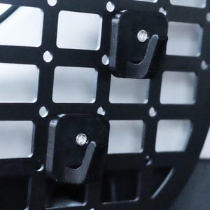 Puede incluir: Dos ganchos de metal negro unidos a una pared de rejilla de metal negro. Los ganchos están diseñados para sujetar objetos en la pared.