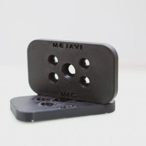 Puede incluir: Placa de plástico negro con varios agujeros y el texto "MOJAVE" y "MFG" impreso en ella.