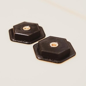 May include: Two black hexagonal camera tripod mounts with a threaded hole in the center.