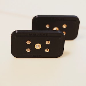 Puede incluir: Dos conectores eléctricos rectangulares negros con terminales de color dorado y el texto "MOJAVE MIG" impreso en el conector inferior.