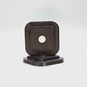 Puede incluir: Un soporte de cámara de plástico negro con el texto "MOJAVE" impreso en él.