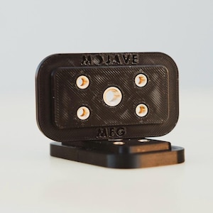 Puede incluir: Un conector de plástico negro con el texto "MOVAVE MFG" impreso en él. El conector tiene cinco agujeros, cuatro de los cuales son más pequeños y uno de los cuales es más grande.