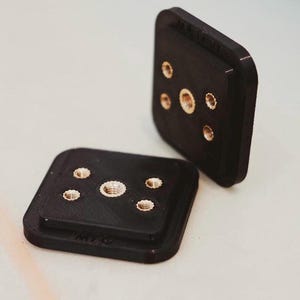 Puede incluir: Dos cuadrados de plástico negro con varios agujeros y un tornillo de latón en cada agujero. Los cuadrados están diseñados para montaje.