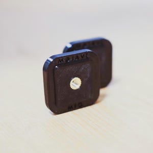 Puede incluir: Dos placas de montaje de cámara de plástico negro con el texto "MOJAVE MFG" impreso en ellas.