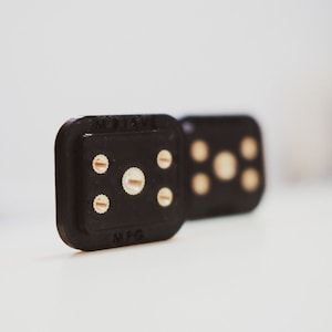 Puede incluir: Dos dados negros con puntos dorados. Los dados están apilados uno encima del otro. El dado superior tiene cuatro puntos y el dado inferior tiene cinco puntos. Los dados están etiquetados con "MOLEX" y "MFG".