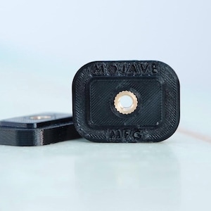 Puede incluir: Dos soportes de cámara de plástico negro con un agujero roscado en el centro. Los soportes están etiquetados como "GoPro Wave" y "M6S".