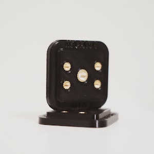 Puede incluir: Un conector de plástico negro con cinco pines de color dorado. El conector está diseñado para conexiones eléctricas.