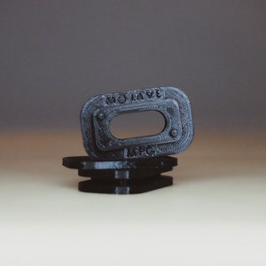 Puede incluir: Dos piezas de plástico negro con el texto "HOLIDAY MFG" en la pieza superior. La pieza superior tiene una abertura rectangular.